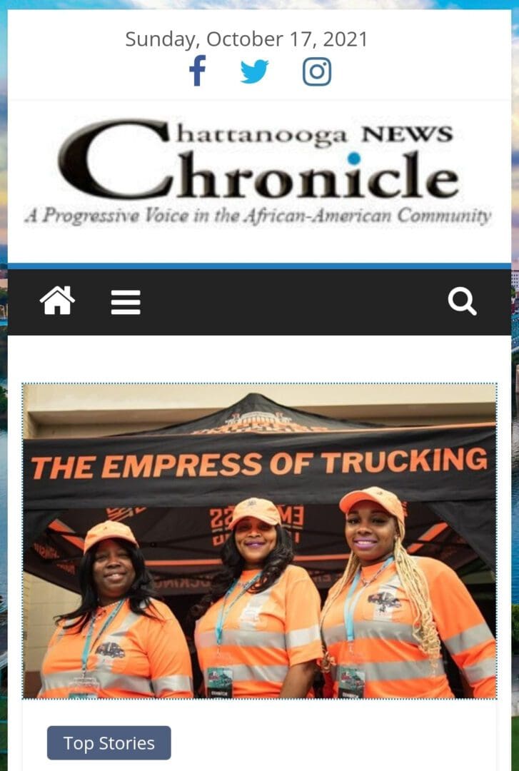 Three women in orange shirts standing next to a black banner.