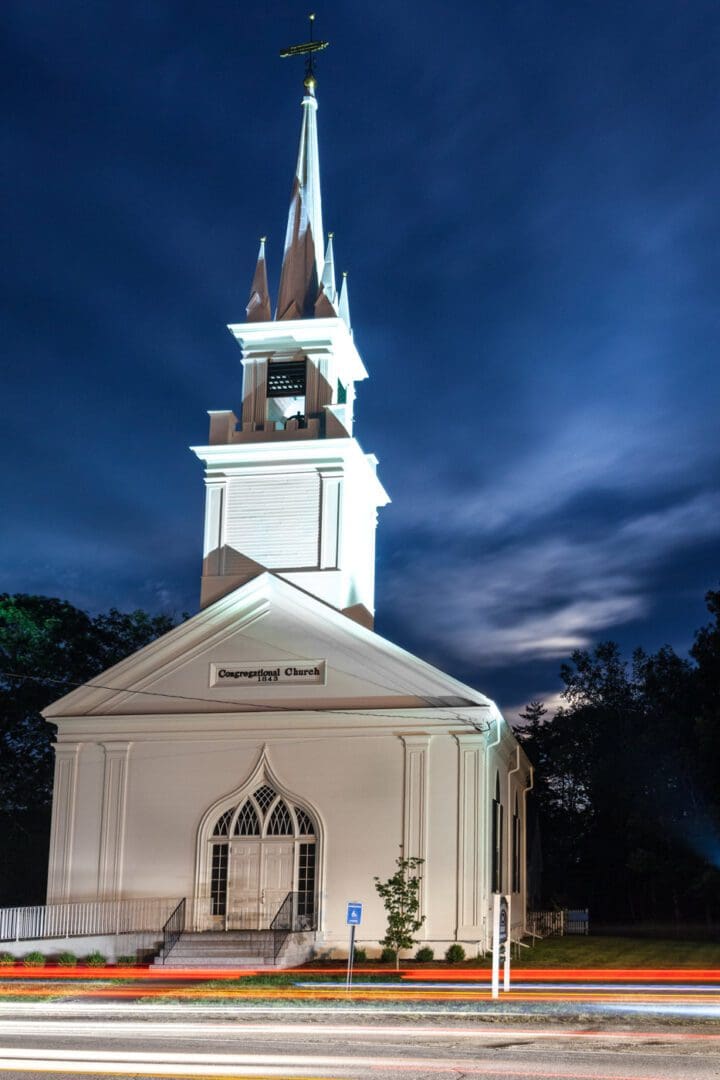 A church with a steeple and clock at night.