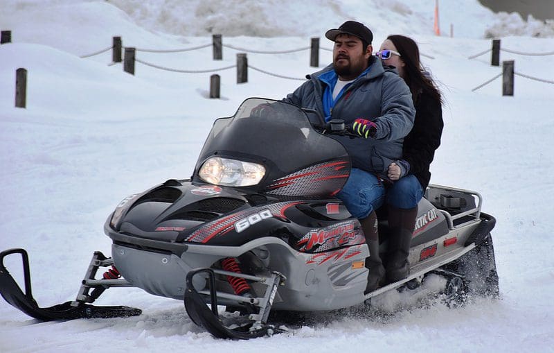 A man and woman riding on the back of a snowmobile.